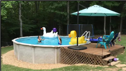 A backyard above-ground pool with inflatable swan and duck floats, kids swimming, and a wooden deck with an umbrella and chairs.