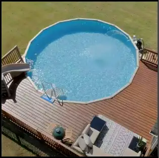 An aerial view of a round above-ground pool set into a wooden deck with a pool skimmer net leaning against the rail.