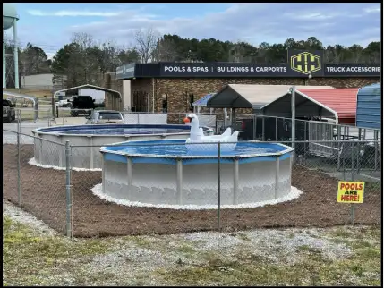Two above-ground pools with a swan float set up on a gravel lot outside an H&H Truck and Outdoor store with a Pools Are Here sign.